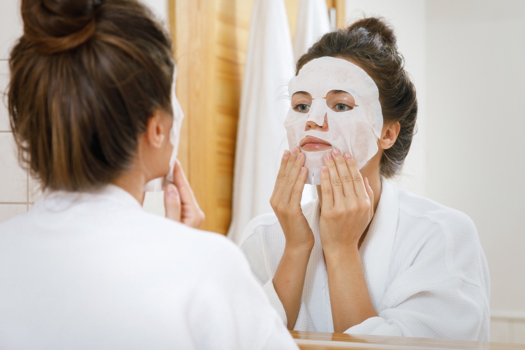 Woman is applying sheet mask on her face