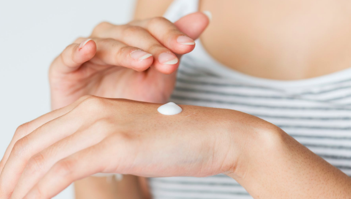 Woman about to apply moisturiser from hand. Image from Pexels.