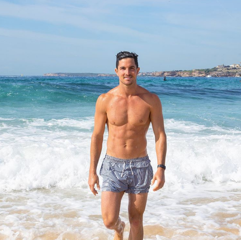Man on the beach in front of waves wearing light blue shorts