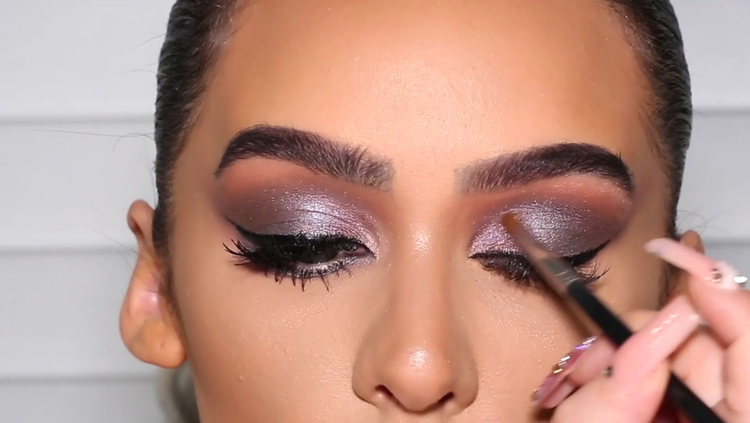 woman applying purple eyeshadow on eyelid with brush.