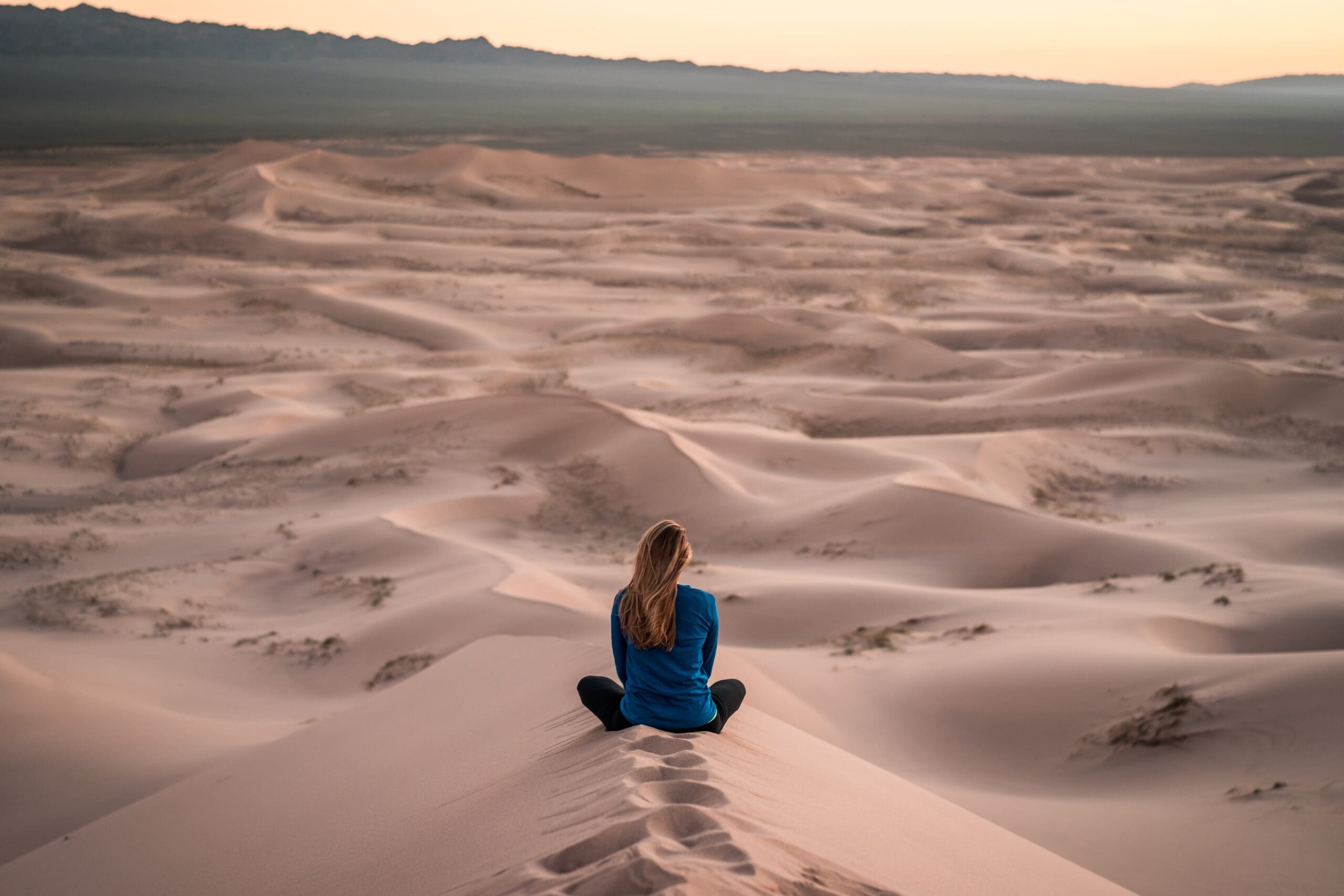 Female meditating on sand dunes.