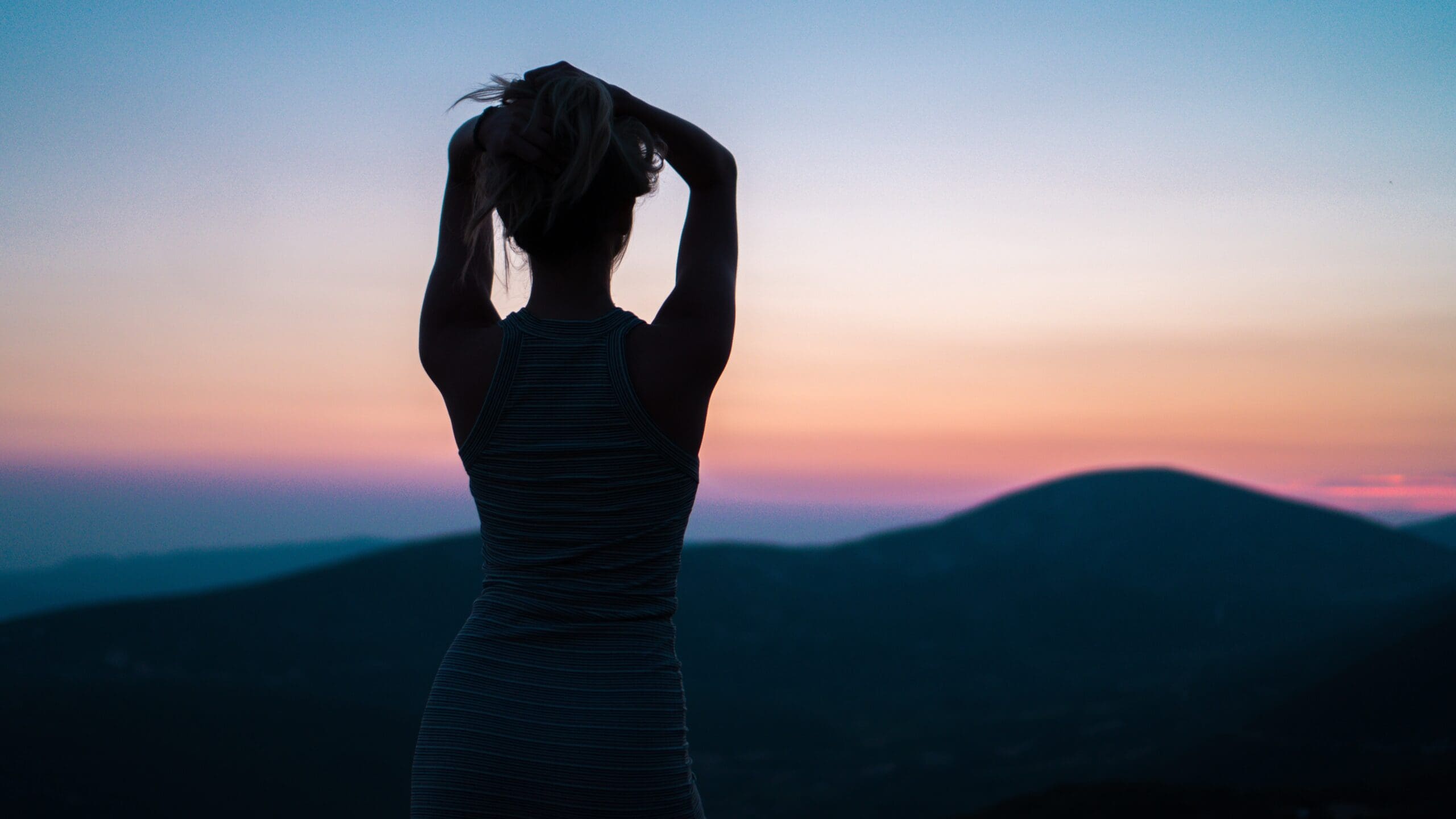 Female silhouette with arms placed above head, looking at sunset view across the mountains.