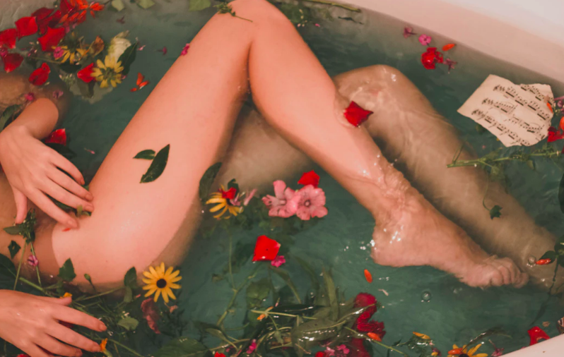 Bare skinned legs in bath filled with flowers