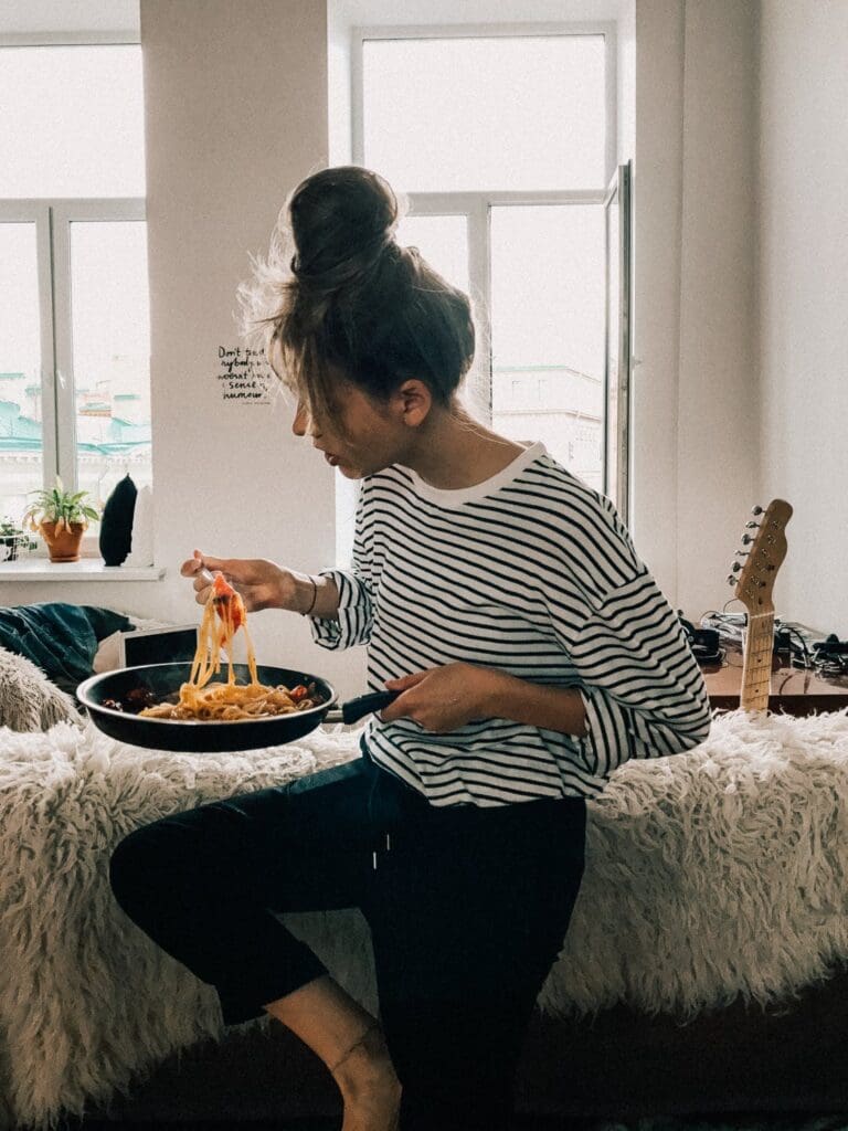 woman cooking at home and eating pasta from a pan