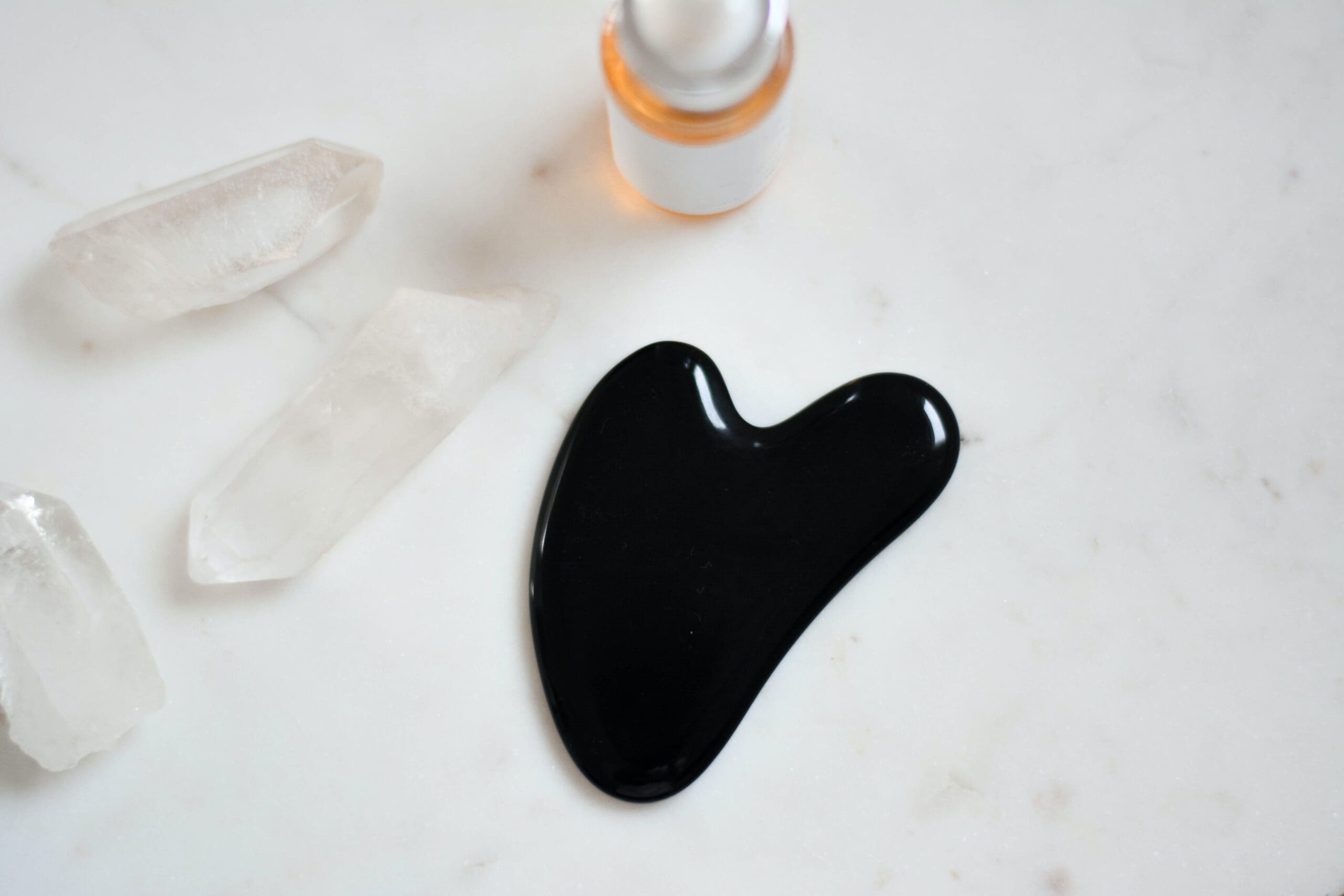 Gua Sha tool surrounded by crystals and face oil.