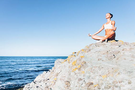 This image is a woman meditating on a rock near the ocean.