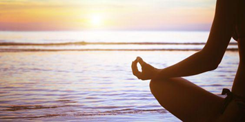 Making Meditation Mainstream. A woman meditating on the beach an sunrise.