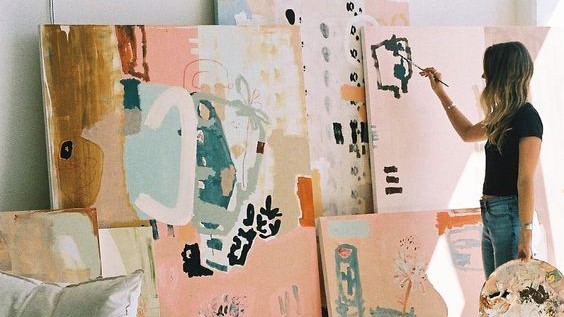 Woman painting several abstract pastel canvases.