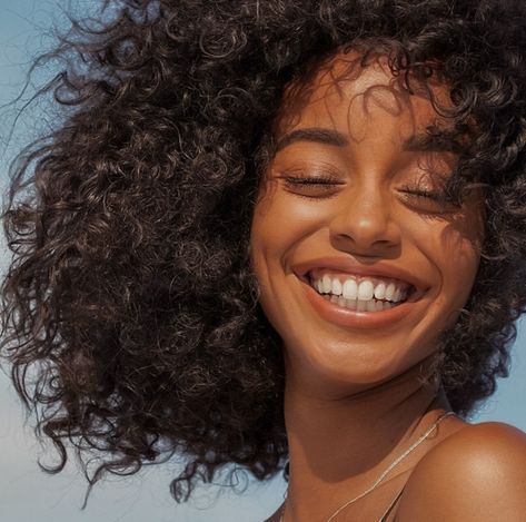 A black woman with afro hair and white teeth smiling. Eyes closed.