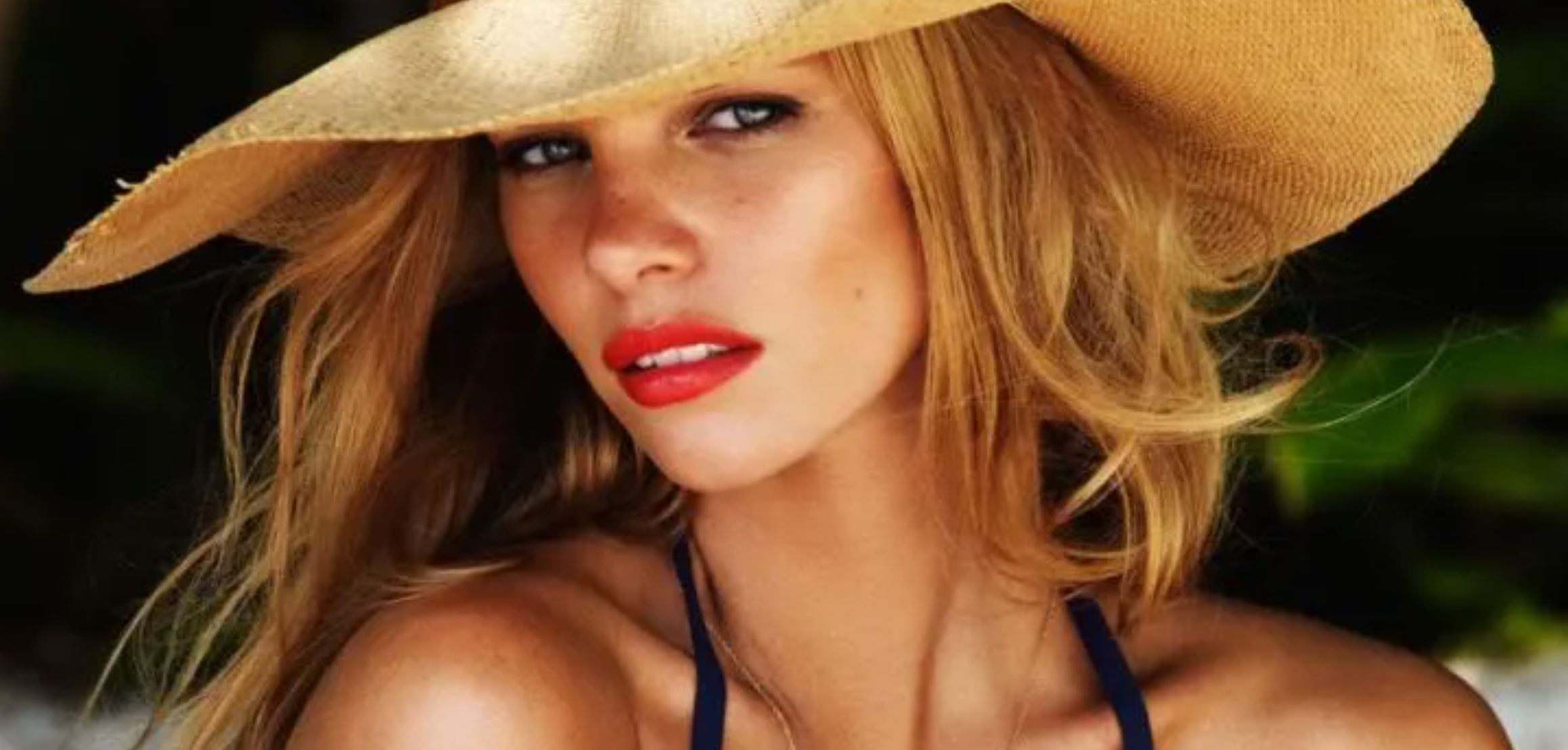 A woman wearing red lipstick, a bikini and wide brimmed hat