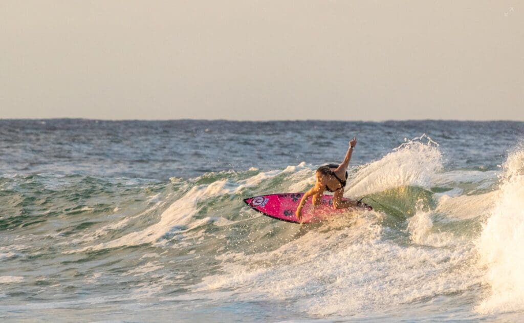 A female surfer on a pink board catching a wave. 