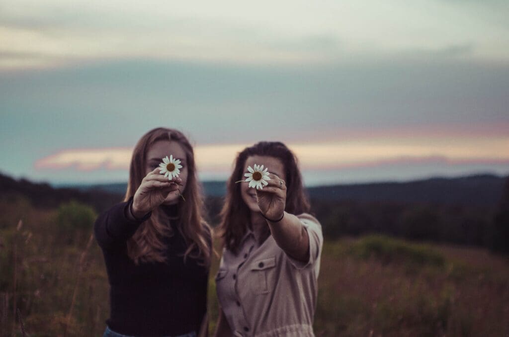 two women hold up daisy flowers