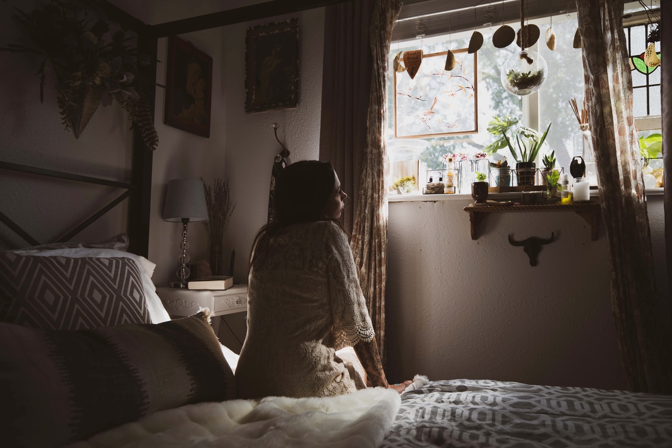 woman sitting on her bed staring out her window